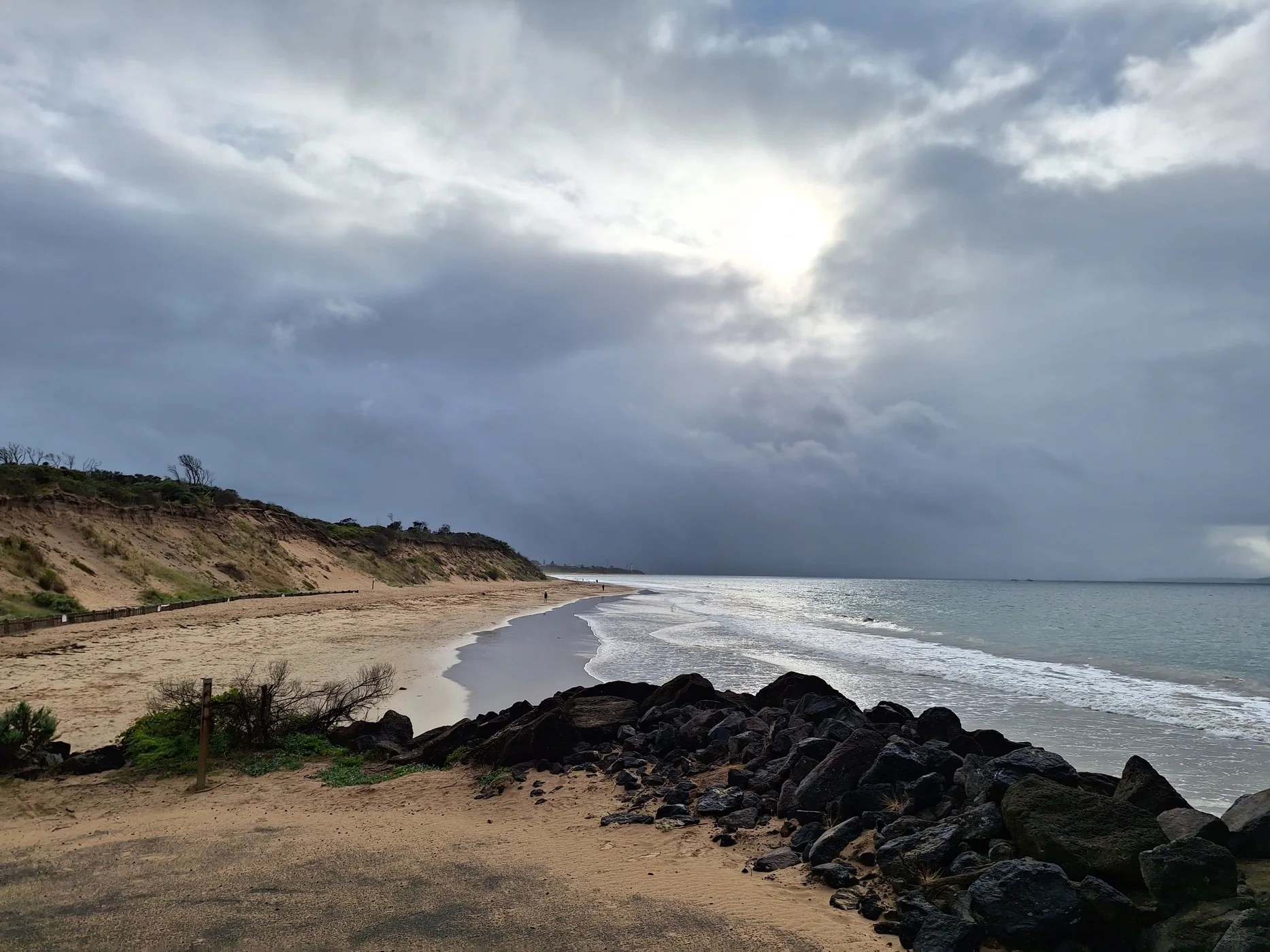 A quiet beach beneath dramatic clouds with sunlight breaking through